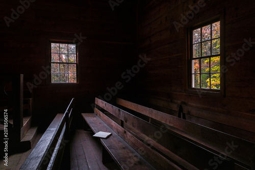 Cuadro en lienzo Dark interior of a church with a bible on a pew and fall foliage visible through