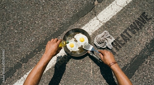 Top Down View of Hands Frying Eggs in Pan on Hot Asphalt Road with Heatwave Text as Global Warming Metaphor