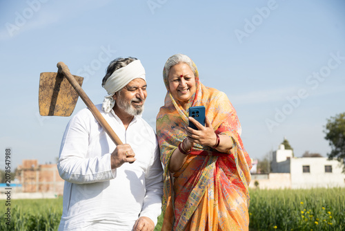 Senior Indian farmer couple smart phone at agricultural field, man holding a spade, showing digital technology, rural lifestyle, and modern farming in India