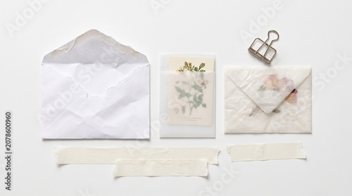 Elegant white translucent paper envelopes, a delicate botanical illustration card, and a silver binder clip. Minimalist stationery set for wedding invitations, personal correspondence