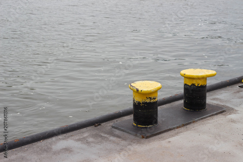 Canvas-taulu Two yellow and black mooring bollards positioned on a concrete dock beside calm