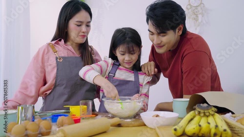 Happy Asian family mixing flour dough together to bake dessert in kitchen