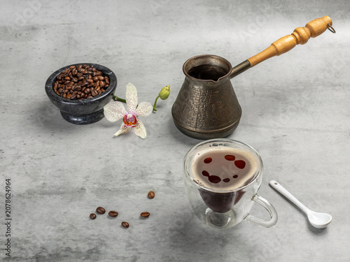 Cup of coffee, a stone bowl with roasted coffee beans and a cezve.