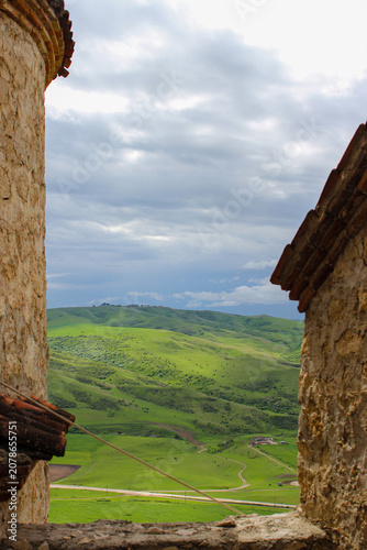 A view of the valley and green meadows from the monastery wall. Mountains and clouds in the background. Elia, Kakheti, Georgia