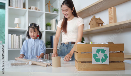 Smiling Asian mother and daughter sorting plastic bottles for recycling at home