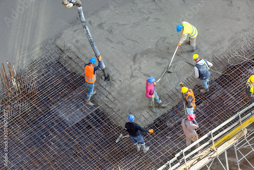 Billede på lærred Construction workers pouring concrete on a reinforcement steel bar grid for a mo