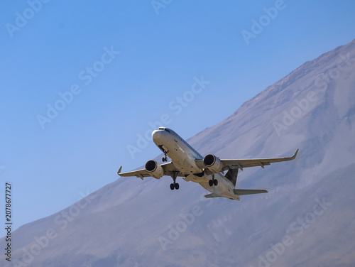 White twin-engine commercial plane approaching runway with volcano behind