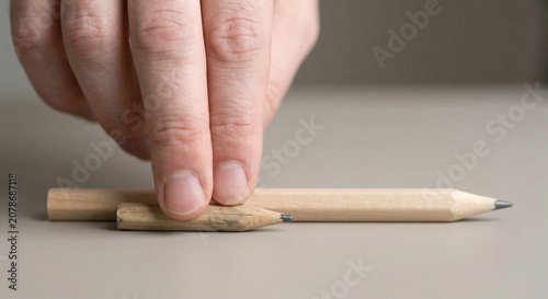 Close up of fingers holding an extremely short wooden pencil stub next to a standard long pencil for comparison