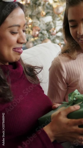 Vertical video: Offering child presenting green gift on sofa for Christmas, mom reacting, smiling