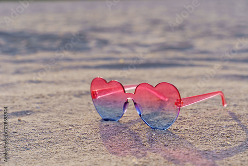 Pink heart shaped sunglasses on sandy beach near sea