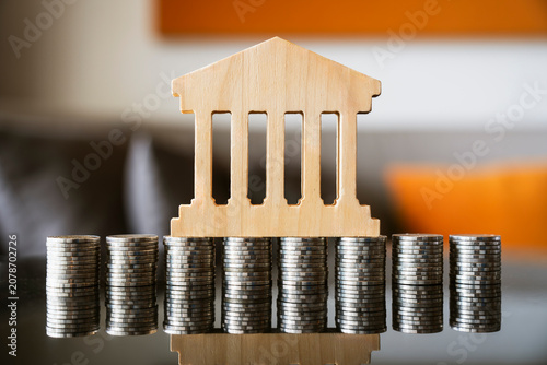 Bank wooden model on stacked coins for dollar cost averaging DCA investment plan concept, long term financial savings asset management, banking foundation stability, capital growth analysis.