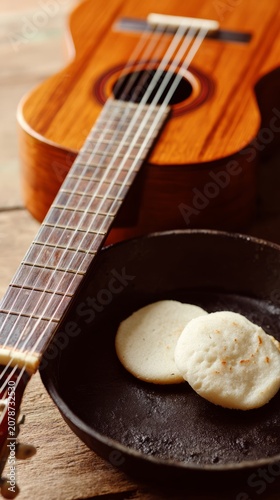 Arepas on cast-iron griddle beside cuatro guitar, tropical culinary and music scene.
