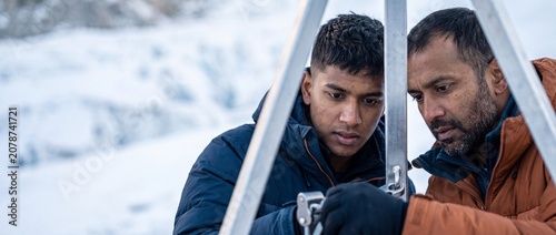 Glacier research scientists operating equipment on snowy mountain during polar expedition, focused male geologic researchers wearing winter jackets analyzing climate change data in freezing cold weath