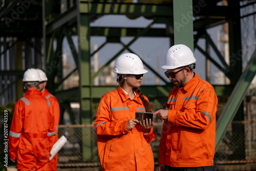 Engineers discussing plans using tablet at refinery