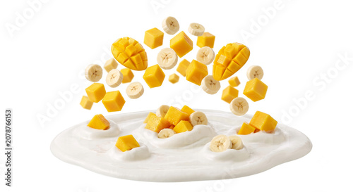 Distant shot of mango cubes and banana slices falling into thick yogurt cream with a clean splash