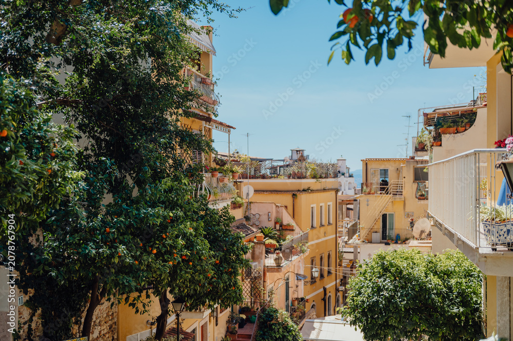 Fototapeta premium Charming Italian street view with lush orange trees in Taormina