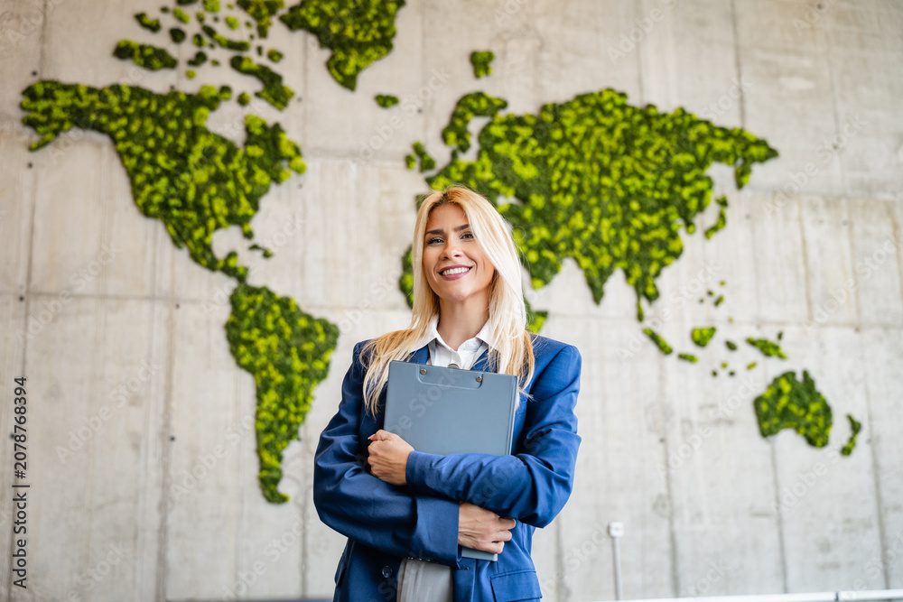 Naklejka premium Businesswoman standing confident with clipboard in front of green world map symbolizing global sustainability