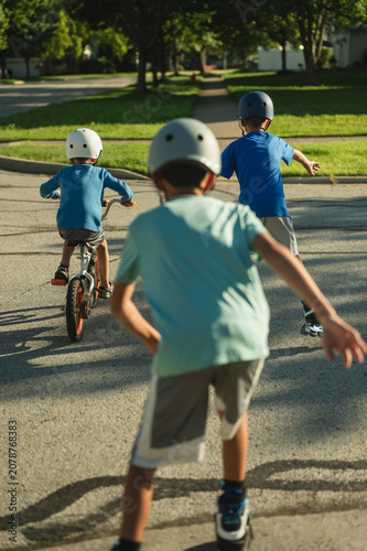 Three young boys biking and skating on quiet neighborhood street