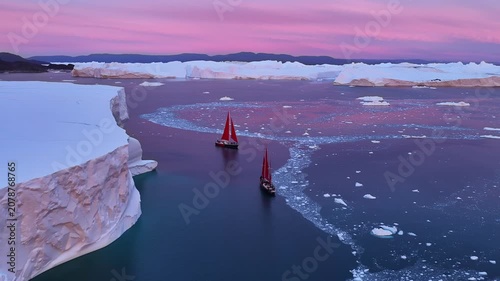 Sailboats with red sails navigating arctic icebergs