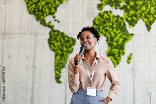 Black woman business speaker presenting at conference with world map backdrop and confident smile