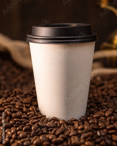 Blank White Disposable Paper Coffee Cup with Black Lid on Roasted Coffee Beans, Vertical Takeaway Cup Mockup for Cafe Branding and Beverage Presentation in a Rustic and Earthy Setting.