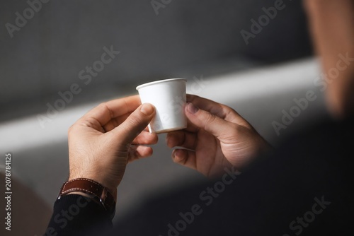 Over the Shoulder View of Hands Holding a Small Blank White Espresso Sample Cup, Miniature Paper Cup Mockup for Coffee Tasting and Branding Presentation in a Moody Cafe Interior.
