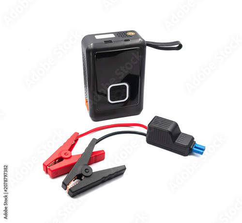  A compact emergency car battery booster power bank shown alongside heavy-duty jumper clamps isolated on a clean white background