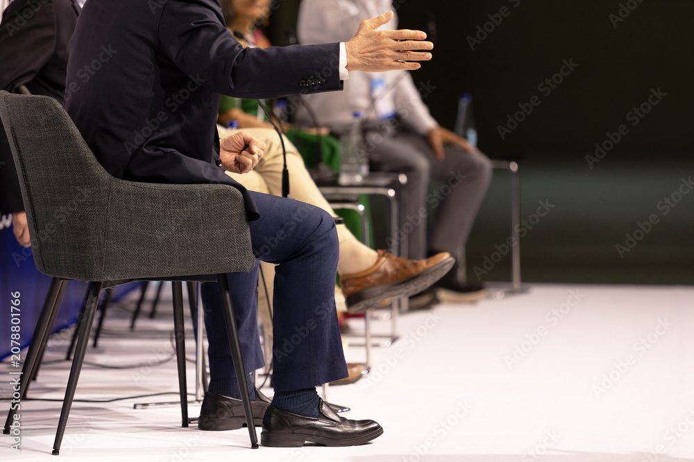 Fototapeta premium Business panel discussion with gesturing speaker and microphones at corporate conference, leadership forum and executive event. Round table political meeting with copy space.