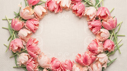 Elegant spring tulip wreath frame with pink flowers on a textured linen background with central copyspace, romantic Mother's Day flatlay design
