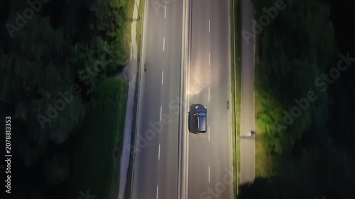 Aerial view of a black car driving on a well-lit road at night, showcasing the smooth flow of traffic with a truck approaching from the opposite direction