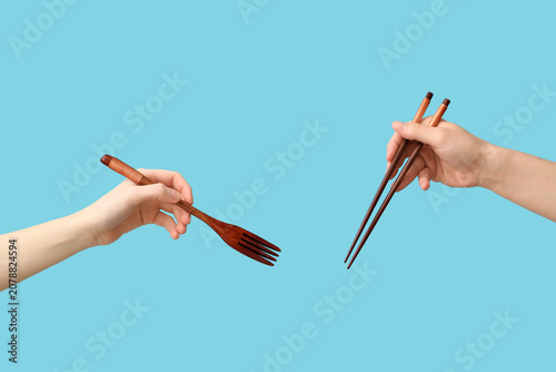 Fotografie Hands holding wooden fork and chopsticks on blue background