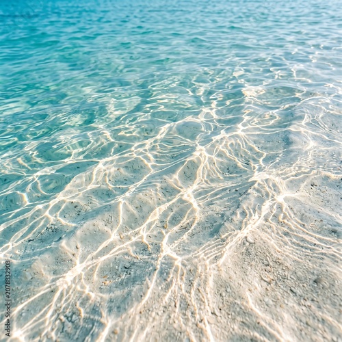 Clear turquoise ocean water with sun reflections on white sandy bottom close up view.
