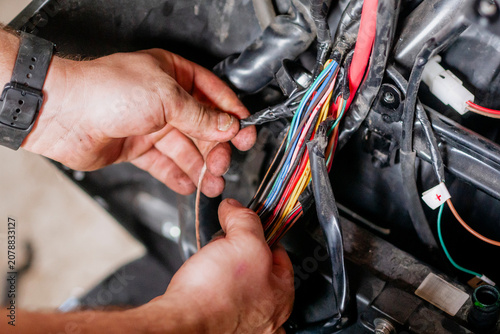 Cropped shot of mechanic hands repairing colorful electrical wiring harness or car loom in garage workshop, vehicle maintenance concept