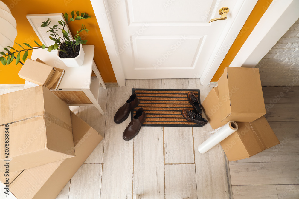 Obraz premium Doormat with shoes and cardboard boxes in hallway on moving day, top view