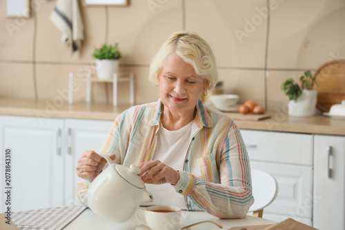 Senior woman pouring tea at table in kitchen
