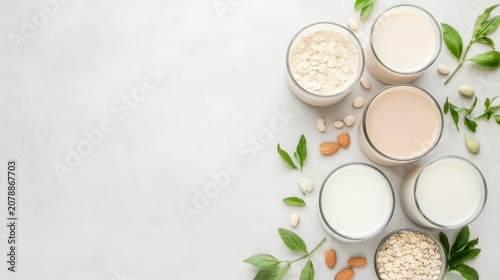 Assortment of plant based milks and ingredients, featuring oat, almond, and soy, presented in glasses with fresh green leaves, conveying healthy natural beverages.