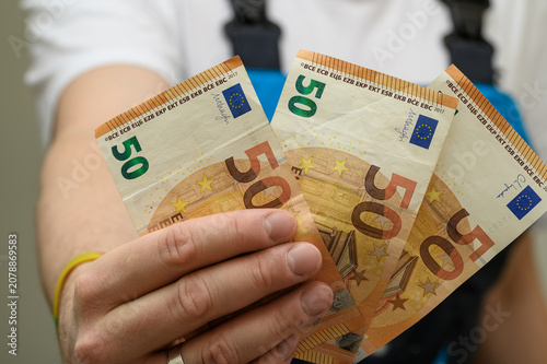 Photography A worker in overalls showing banknotes in his hand, minimum wage for manual labo