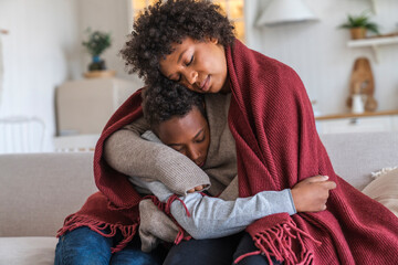 Mother embracing son wrapped in blanket at home