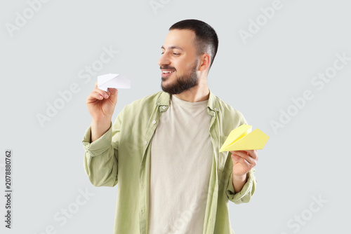 Young man with paper planes on light background