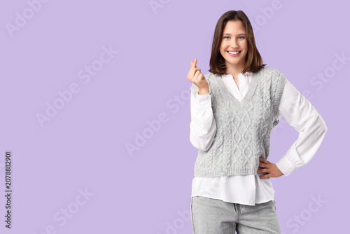 Beautiful young happy woman in stylish grey vest showing heart gesture on pur...