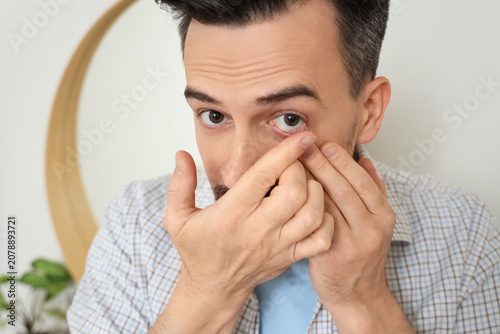 Canvastavla Young man putting in contact lenses at home, closeup