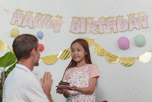 Photography Girl holding birthday cake with father in front of happy birthday banner