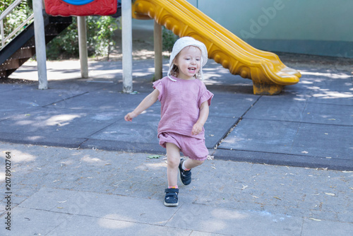 Foto Smiling toddler girl running in front of a playground slide