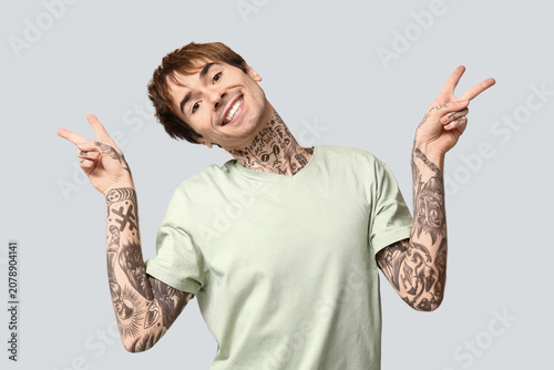 Handsome young man showing victory gesture on grey background