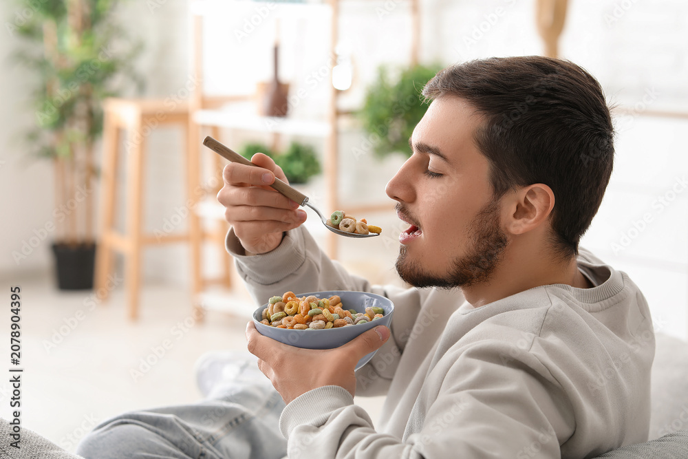 Fototapeta premium Handsome young man eating tasty cereal rings in living room