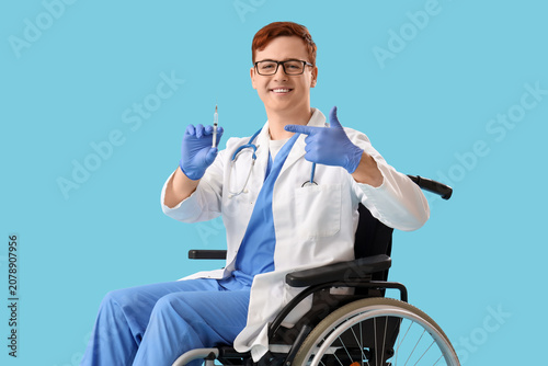 Male doctor in wheelchair pointing at injection on blue background