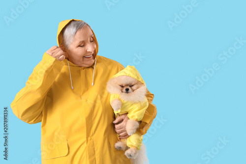 Senior woman in raincoat with Pomeranian dog on blue background