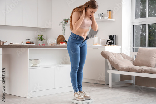 Young woman in tight jeans measuring weight on scales at home