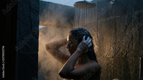 Woman washing hair under hot shower in luxury bathroom with steam