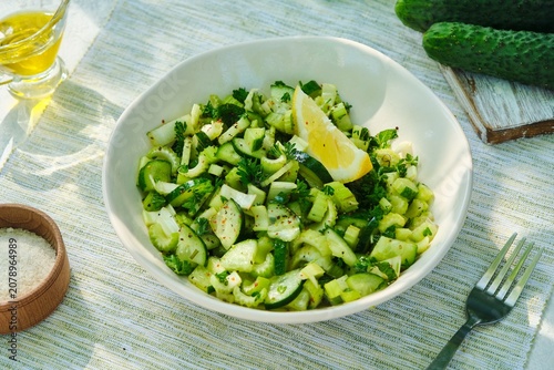 A healthy salad with celery, cucumber, parsley, and a lemon-olive oil dressing in a light bowl on a white concrete background.